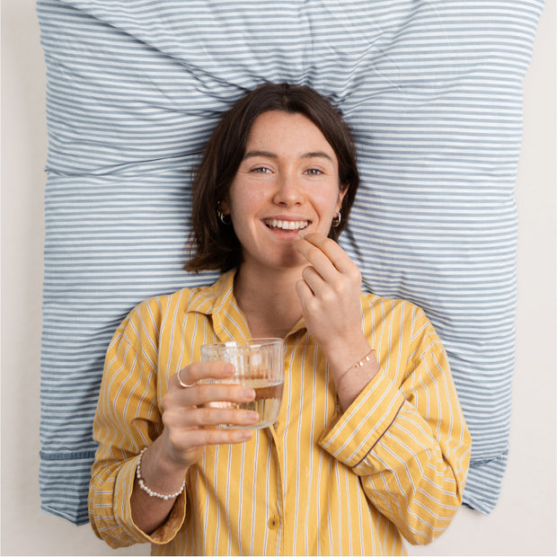 Femme allongée sur un coussin prenant une gélule avec un verre d'eau