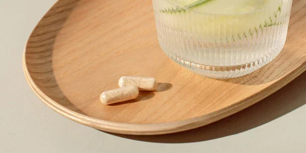 Gélules de vitamine C à côté d'un verre d'eau sur une planche en bois